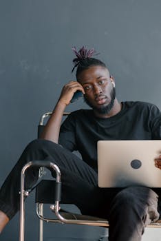 Stylish young man sitting with a laptop, focused on work from home in a modern setting.