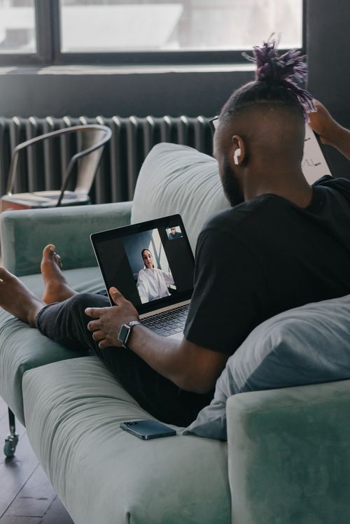 Free A man on a sofa video calling a colleague on a laptop, using earbuds, indoors. Stock Photo