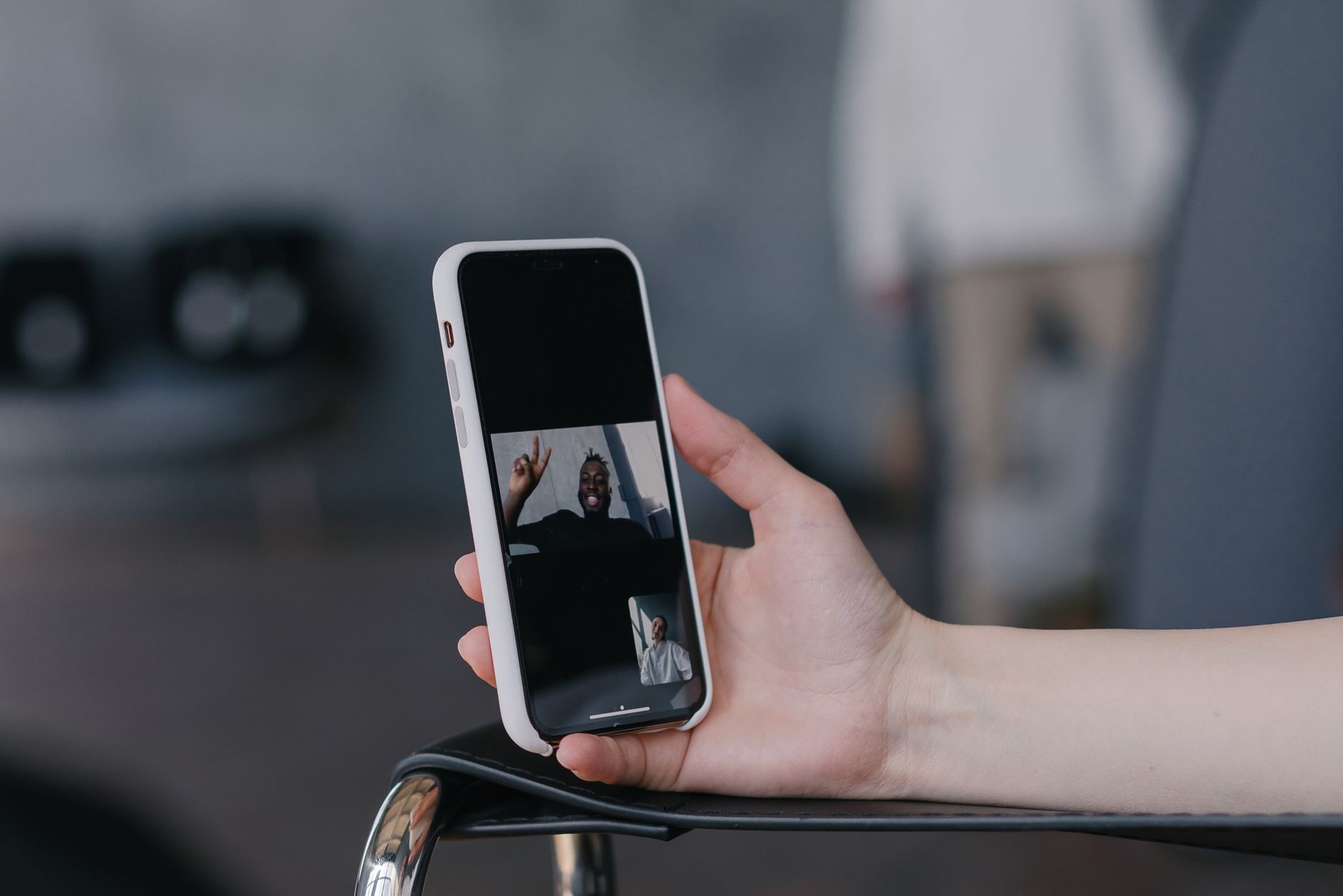 Une main tenant un smartphone affichant un appel vidéo avec deux personnes.