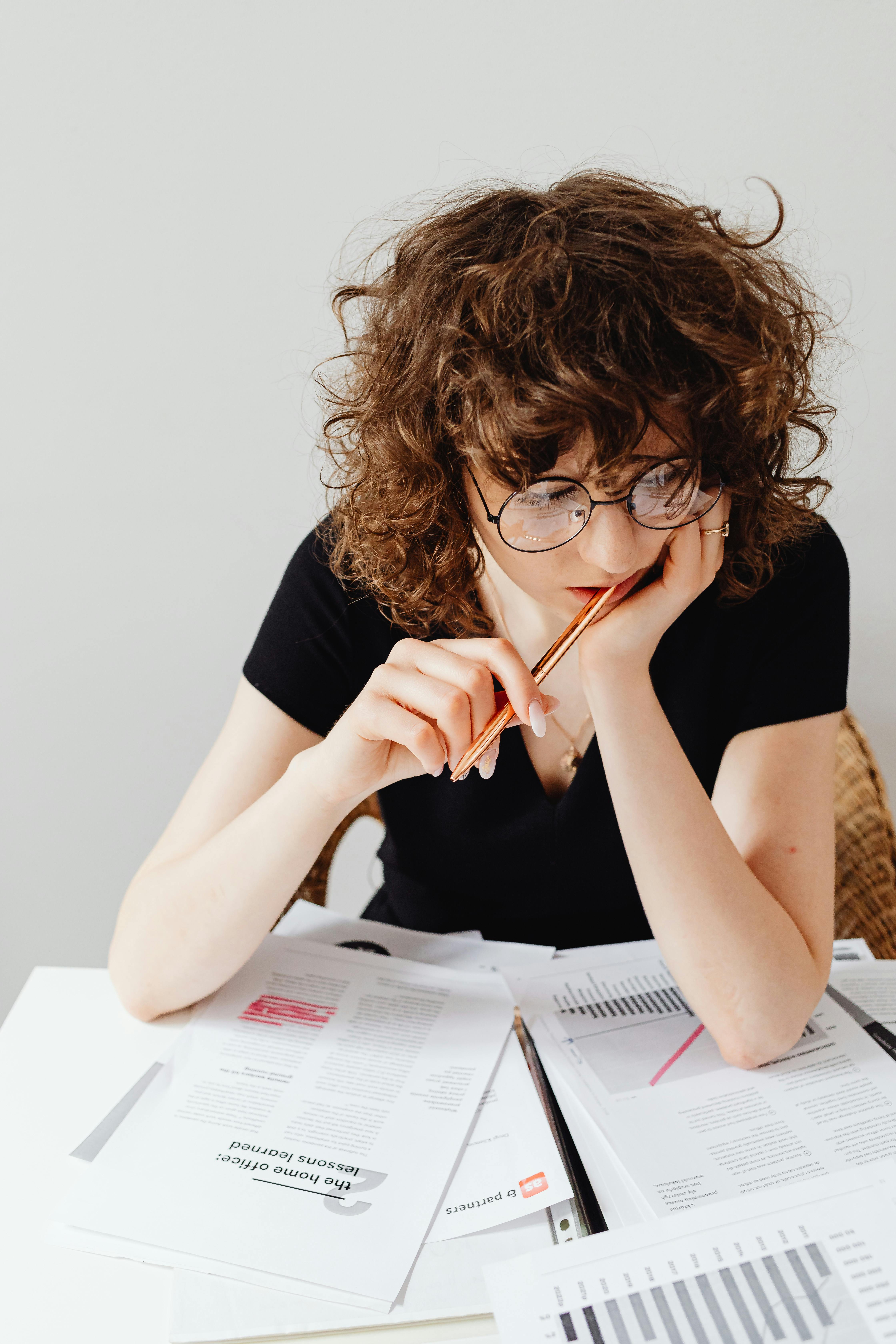 woman in black shirt wearing eyeglasses sitting at table with documents