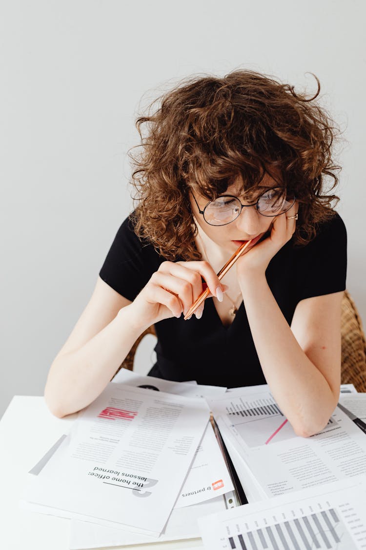 Woman In Black Shirt Wearing Eyeglasses Sitting At Table With Documents