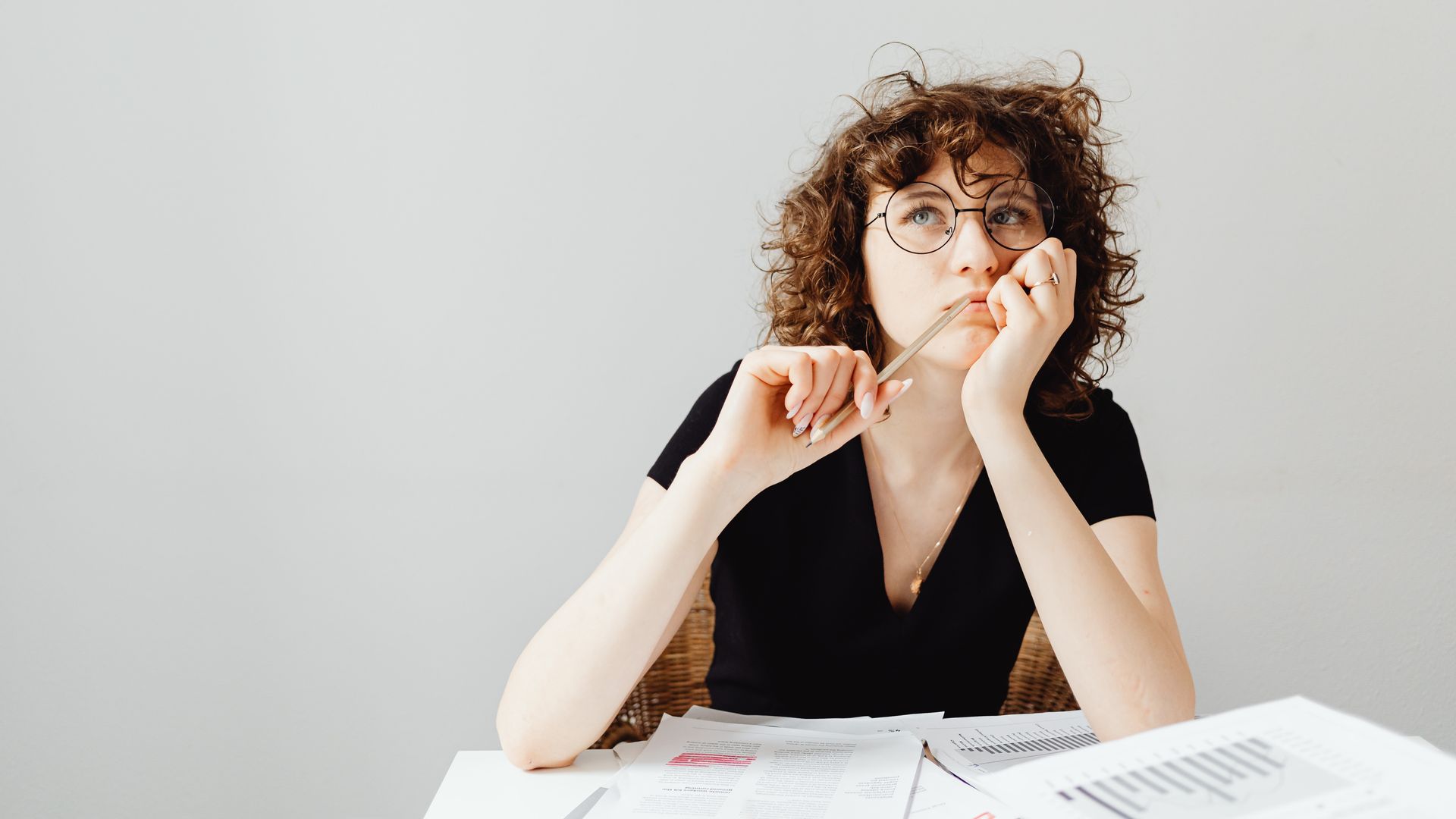 Modafinil Decision Making: A Comprehensive Guide Curly-haired woman with glasses pensively thinking at a desk with documents — modafinil decision making