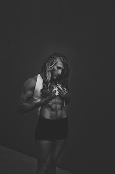 Black and white image of a muscular female bodybuilder posing indoors, showcasing strength and fitness.