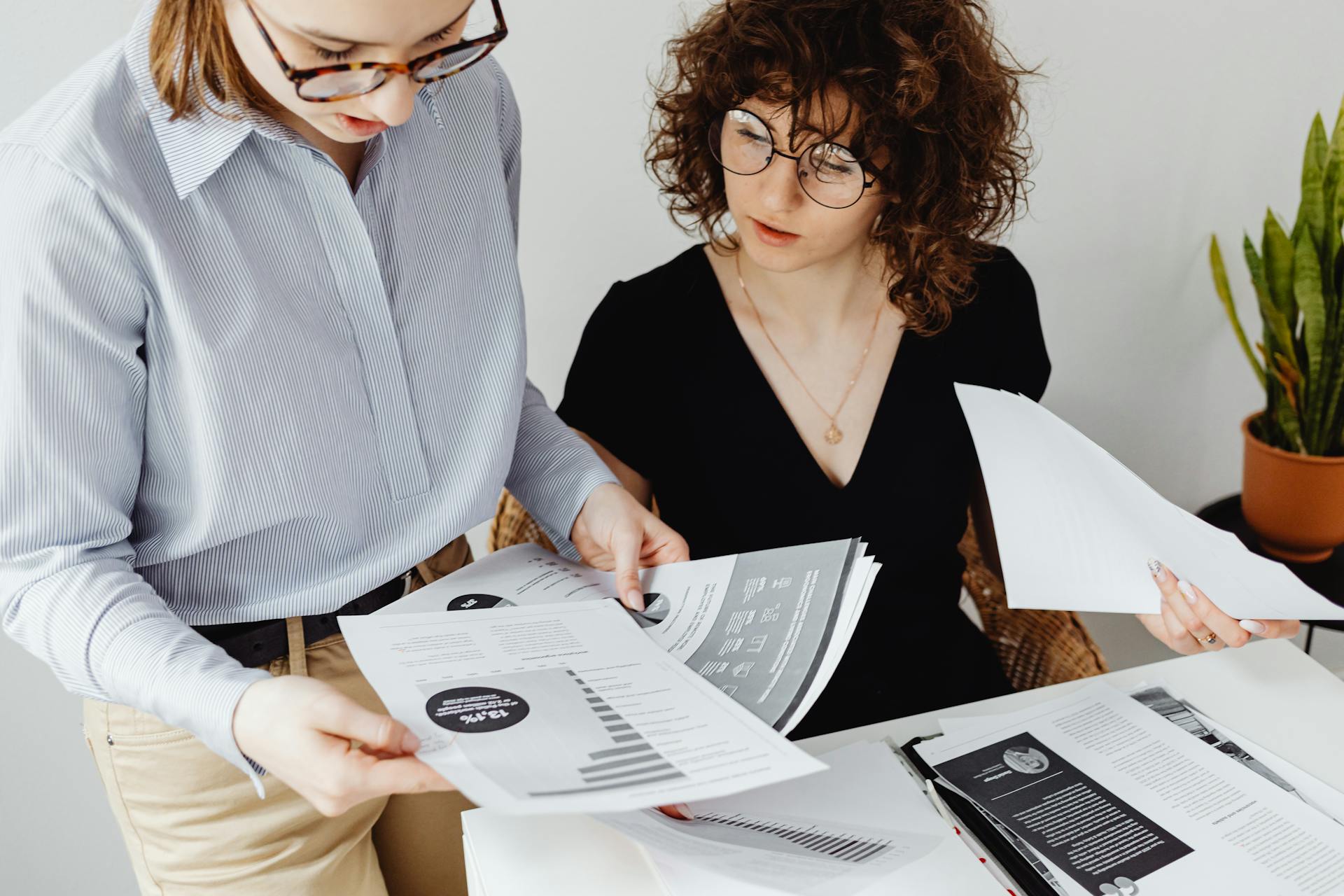 Two women review and discuss financial documents in an office setting, highlighting teamwork and analysis.