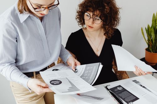 Free Two women review and discuss financial documents in an office setting, highlighting teamwork and analysis. Stock Photo