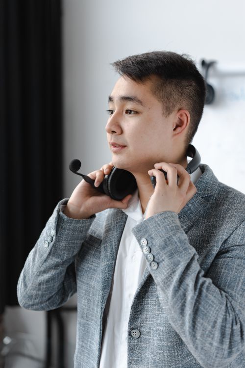 Free Asian man in a gray suit putting on a headset, symbolizing modern customer support. Stock Photo