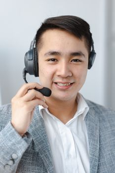 Asian man in formal attire providing customer service with a headset in an office setting.