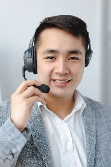 Asian man in formal attire providing customer service with a headset in an office setting.