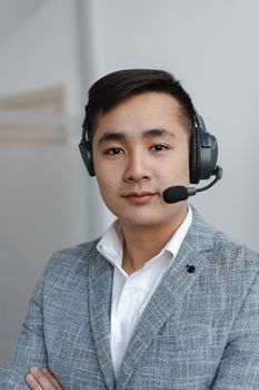 Portrait of a confident Asian call center agent wearing a headset in a modern office environment.