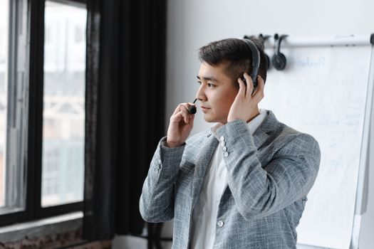Asian male call center agent wearing a headset during a call in an office setting.