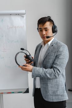 Asian man in business attire wearing a headset, presenting with a flip chart.