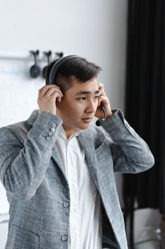 Asian man in a call center wearing a headset, dressed in a gray suit, handling customer service calls.