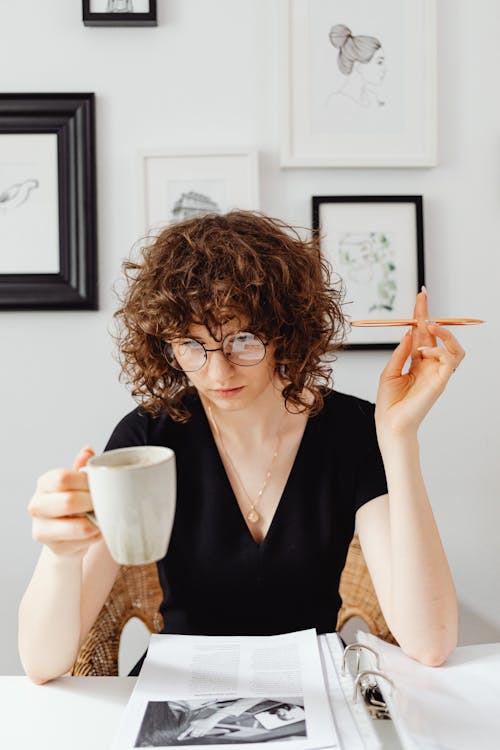 Woman in Black V-Neck Shirt Reading a Document while Holding a Mug of Coffee