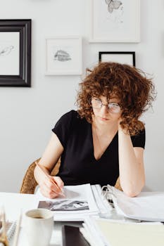 Caucasian woman in black v-neck shirt reviewing documents indoors, with a thoughtful expression.