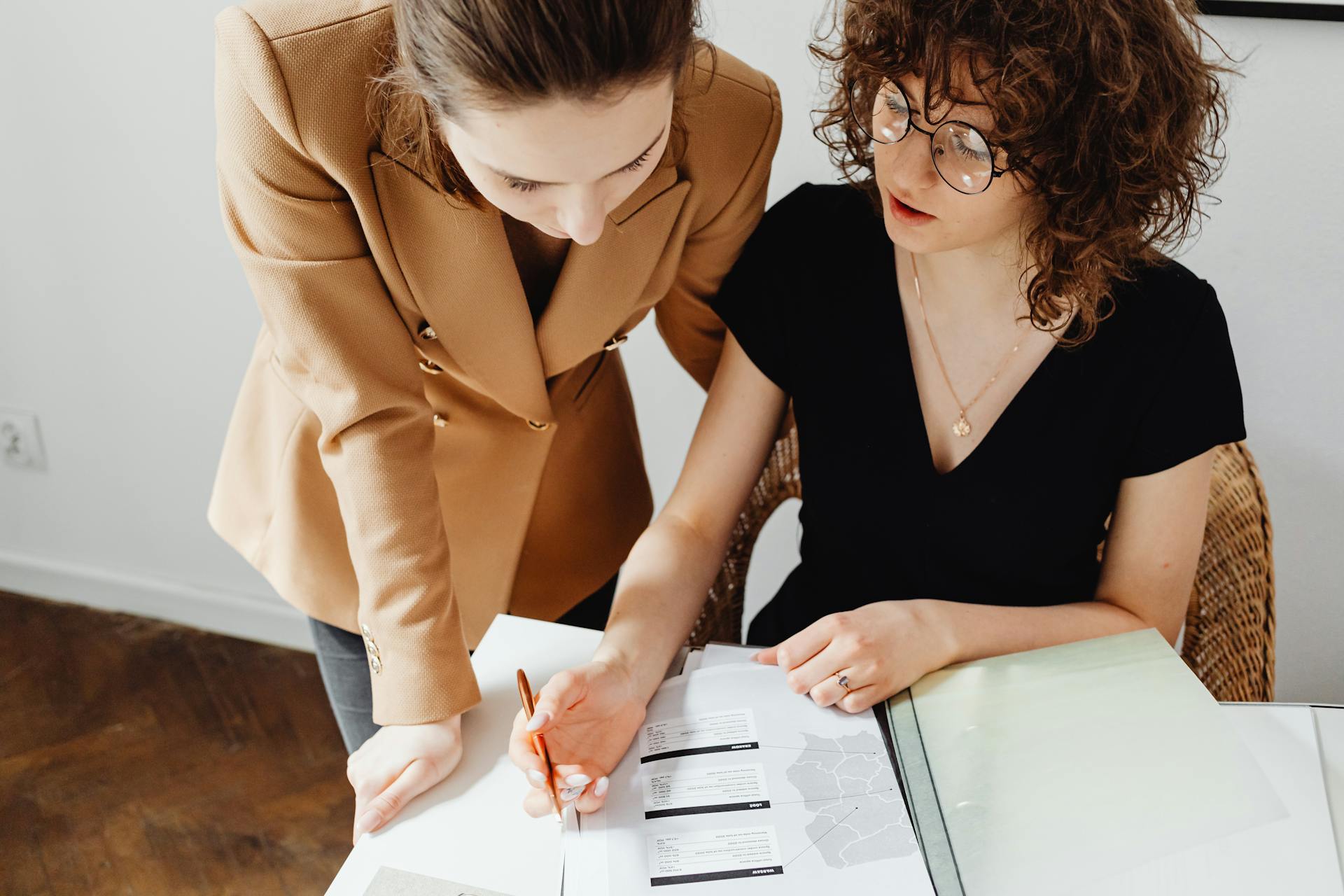 Two women discussing and analyzing business paperwork together in an office setting.