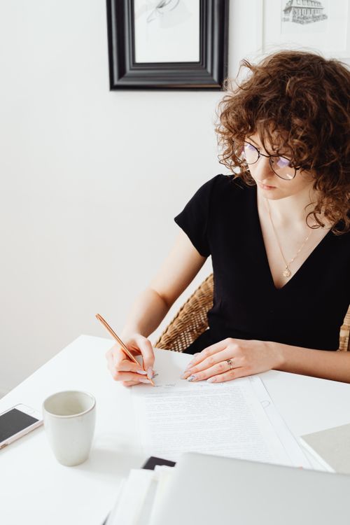 Free A young woman with curly hair writes at a desk in a modern setting. Perfect for work and lifestyle themes. Stock Photo