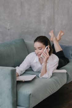 Woman in casual attire multitasking on phone and clipboard at home.