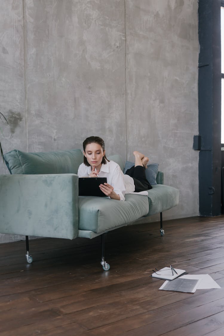 A Woman Lying On A Couch And Using A Tablet