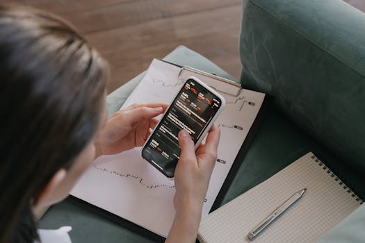 A woman reviews financial data on her smartphone with charts and graphs around her for stock market analysis.