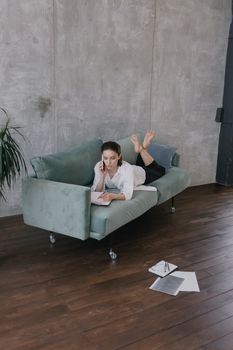 Young woman making phone call while working with documents on a modern sofa in a stylish interior.