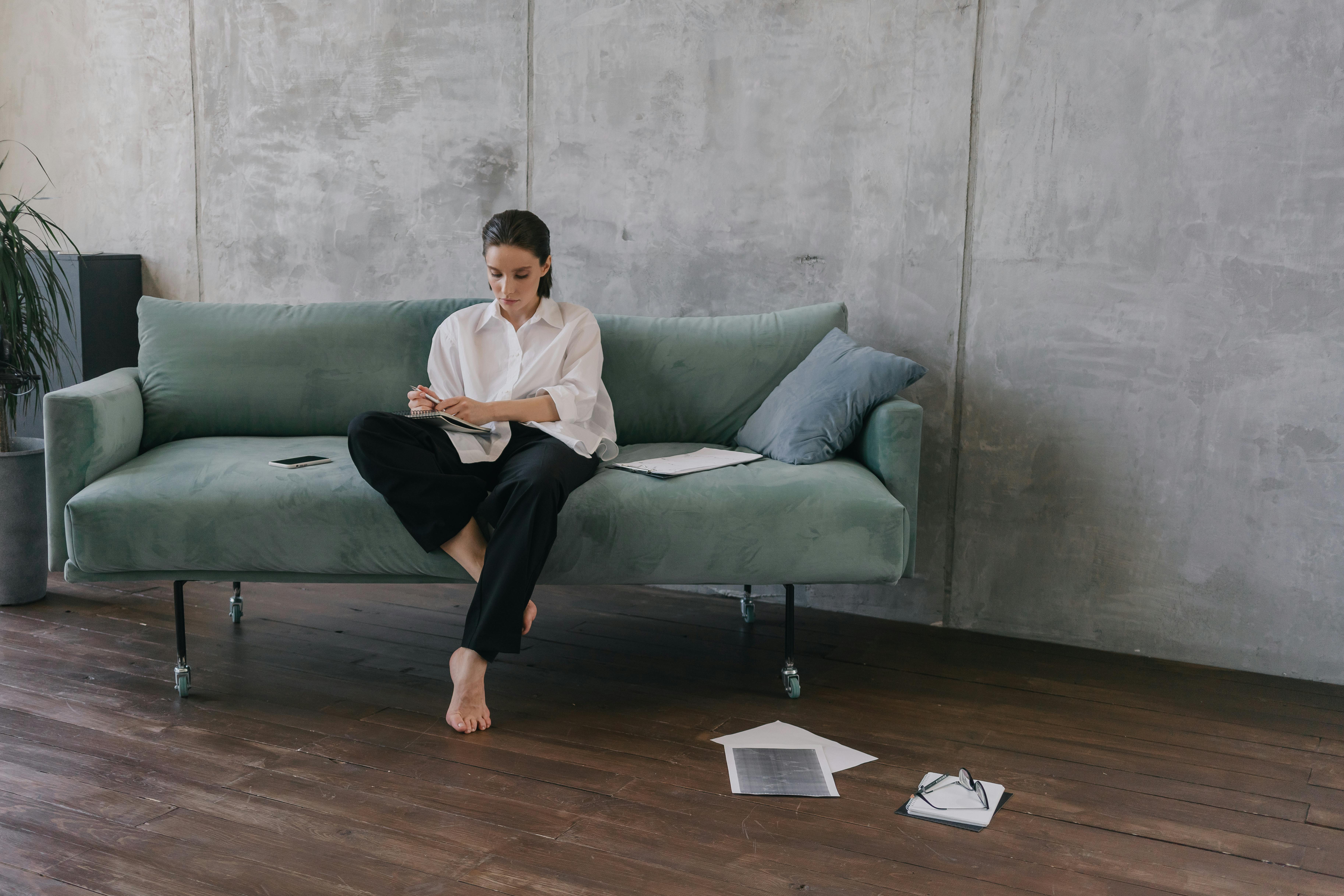 Woman sitting on a couch in an industrial-style living room, engaged in reading or working.