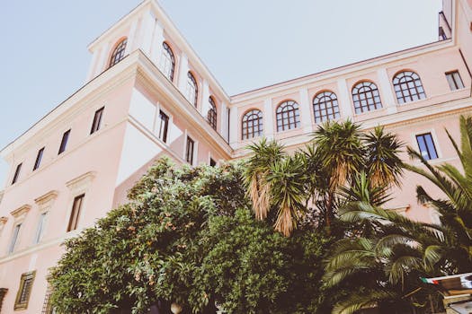 这座优雅的桃色建筑设有拱形窗户，在阳光下映衬着郁郁葱葱的绿色植物