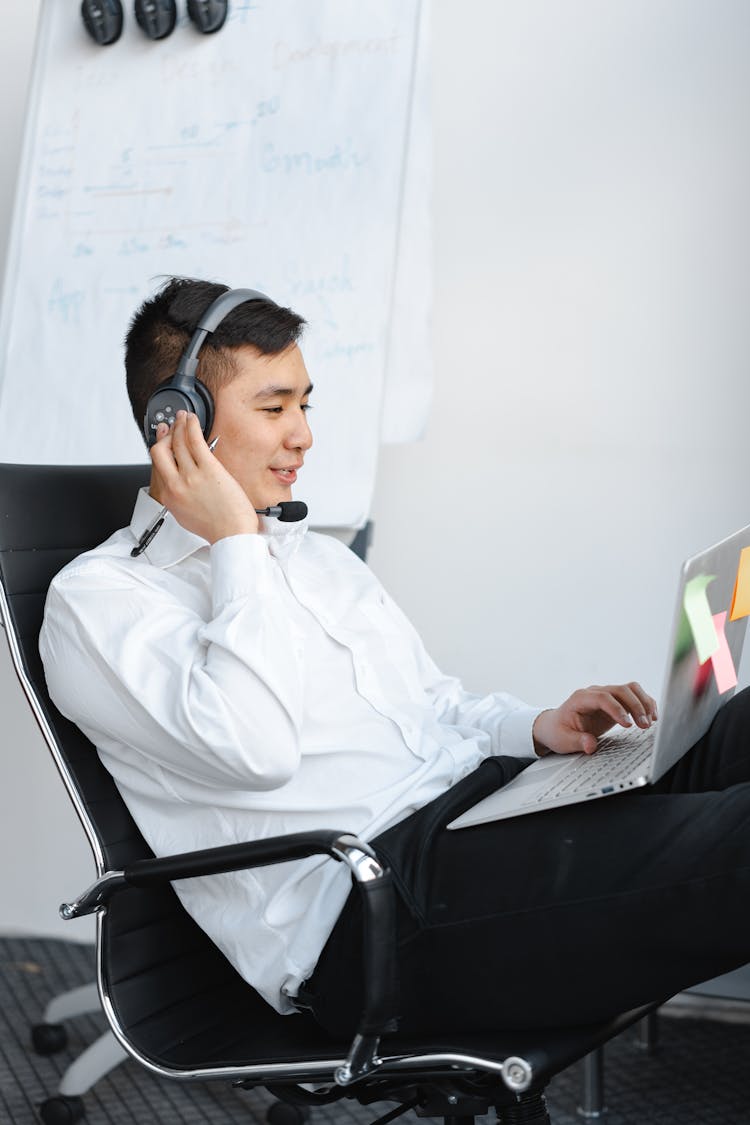 A Man Talking On A Headset While Using A Laptop