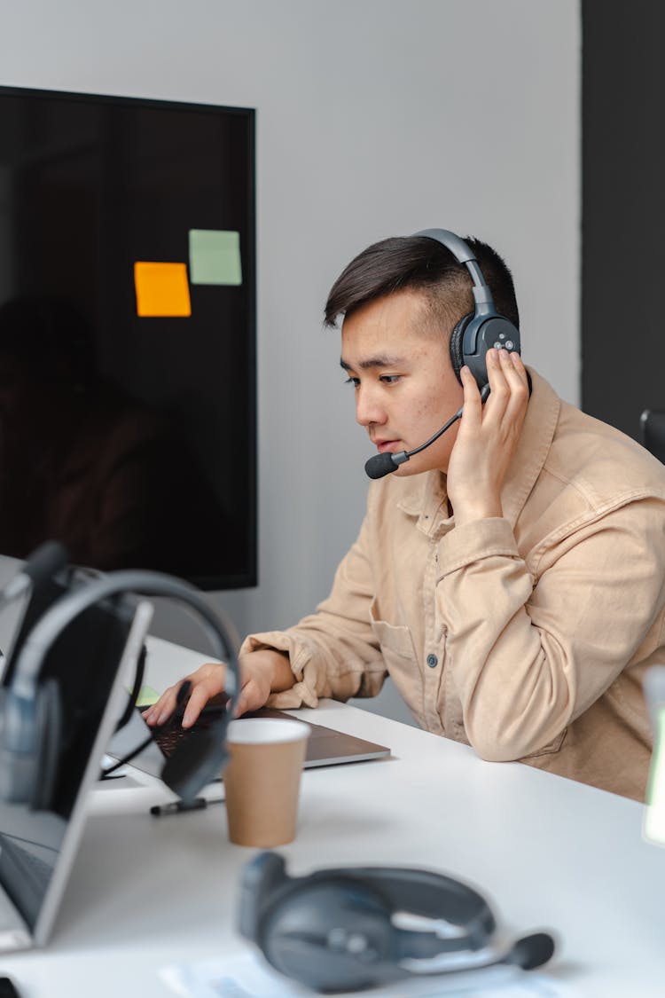 A Man Talking On A Headset While Using A Laptop