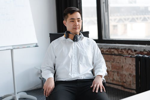 Man in White Dress Shirt and Black Pants Wearing Black Headphones Sitting on Black Chair