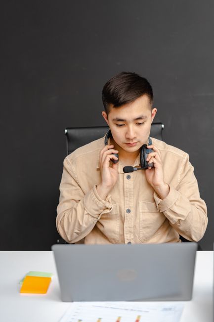 Serious Asian man in call center office, wearing a headset and working on a laptop. Serious Asian man in call center office, wearing a headset and working on a laptop.