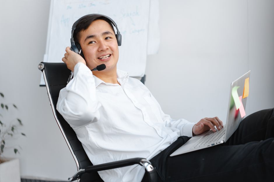 Smiling young man in white shirt using laptop with headset in office setting.