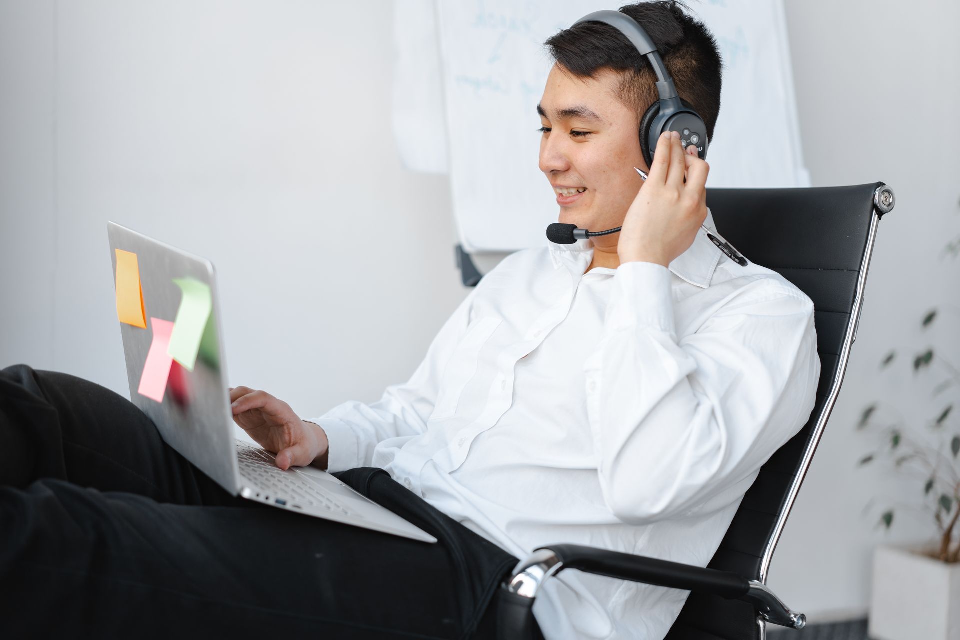 Asian man in office chair with laptop and headset, focusing on a remote work project.