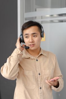 Asian man wearing a headset while holding a smartphone, likely working in customer service or tech support.