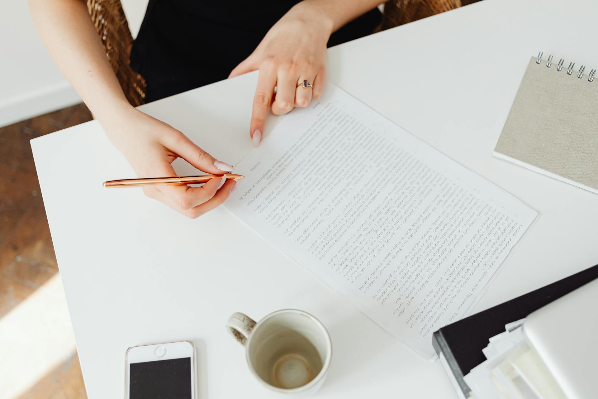 Close-up of a woman reviewing a document at a white desk with a pen.