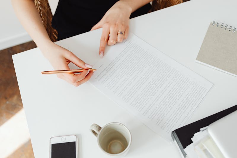 Close-up of a woman reviewing a document at a white desk with a pen.