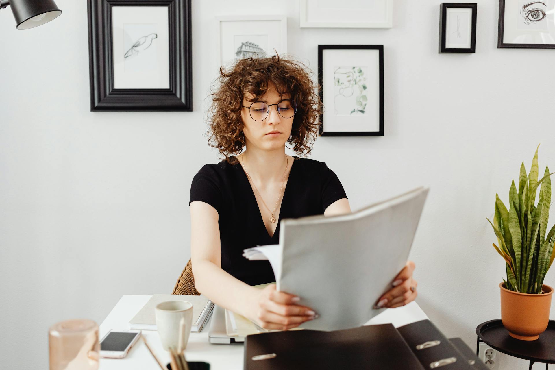 Woman with curly hair and eyeglasses reviewing documents at her desk.