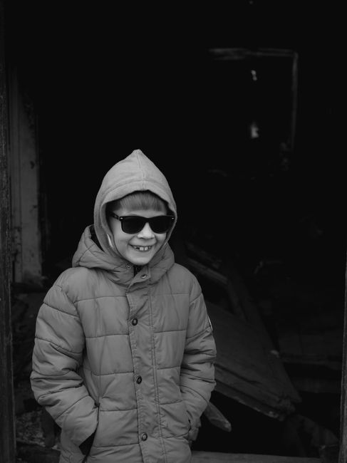 Black and white photo of a cheerful child in a winter coat and sunglasses.