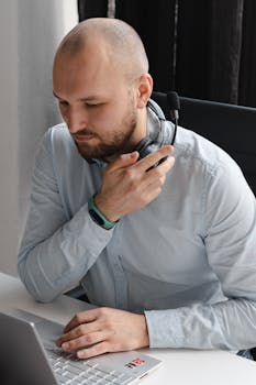 A man with a headset working on a laptop in an office setting.