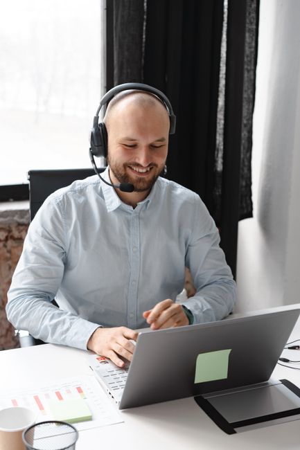 Close-up of a bald man in a call center setting, using a laptop and wearing a headset. Close-up of a bald man in a call center setting, using a laptop and wearing a headset.