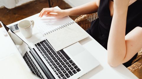 Persona escribiendo en un cuaderno junto a un portátil y una taza de café