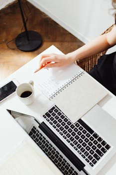 High-angle shot of a workspace with a laptop, coffee, and notebook.