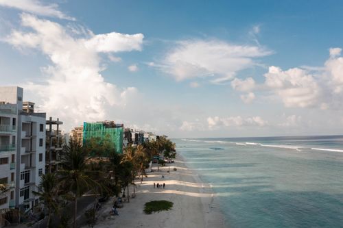 Free Aerial view of a coastal city with beachfront, palm trees, and ocean under a sunny sky. Stock Photo