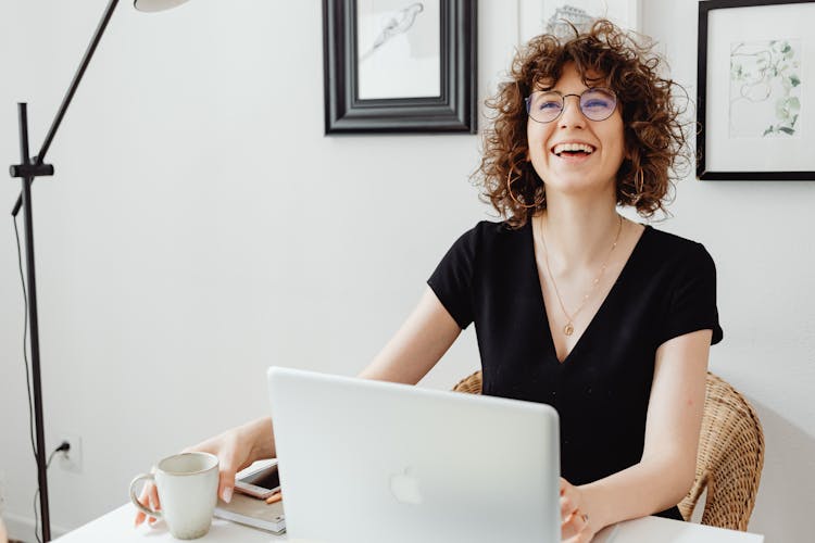 Woman With Curly Hair Laughing Near A Laptop