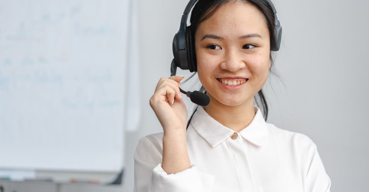 Asian woman smiling in a customer service role wearing a headset indoors.