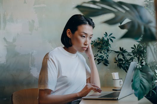 Woman working remotely in a café on her laptop, surrounded by plants.