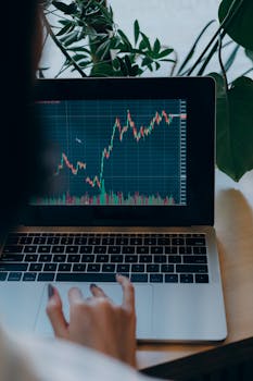 Person using laptop displaying stock market graph amidst indoor plants.