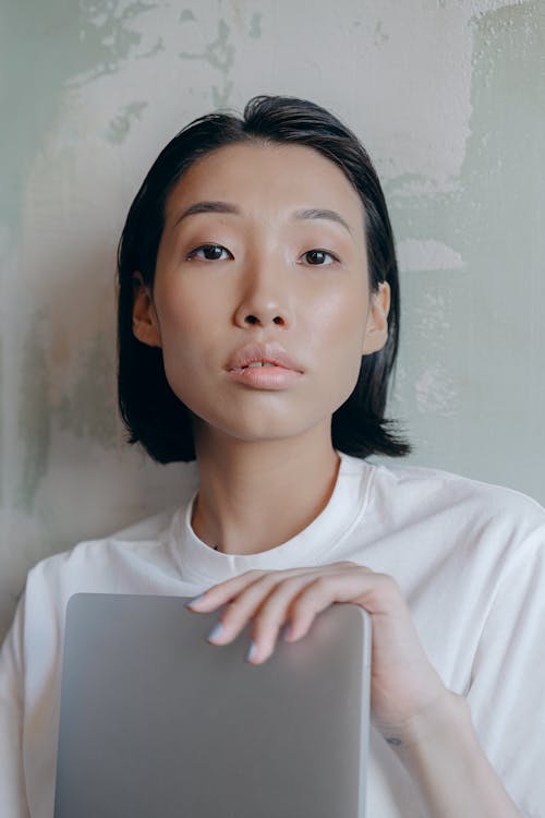 Free Close-Up Photo of a Woman Holding a Silver Laptop while Looking at the Camera Stock Photo