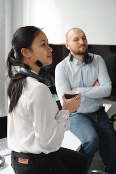Two professionals in casual office wear with headsets, holding a beverage during a casual meeting.