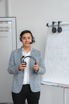 Smiling Asian man with headset in office by flip chart. Ideal for customer service themes.