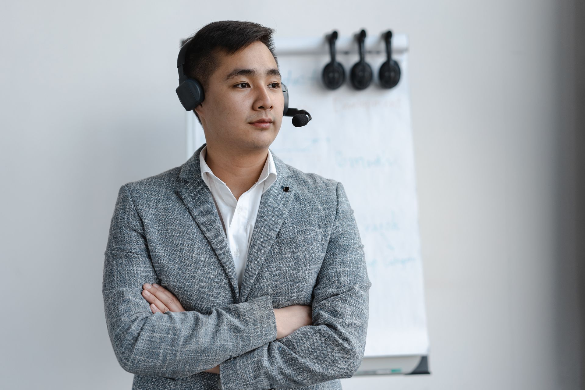 Confident man in headset and gray suit standing indoors, ready for communication and support roles.